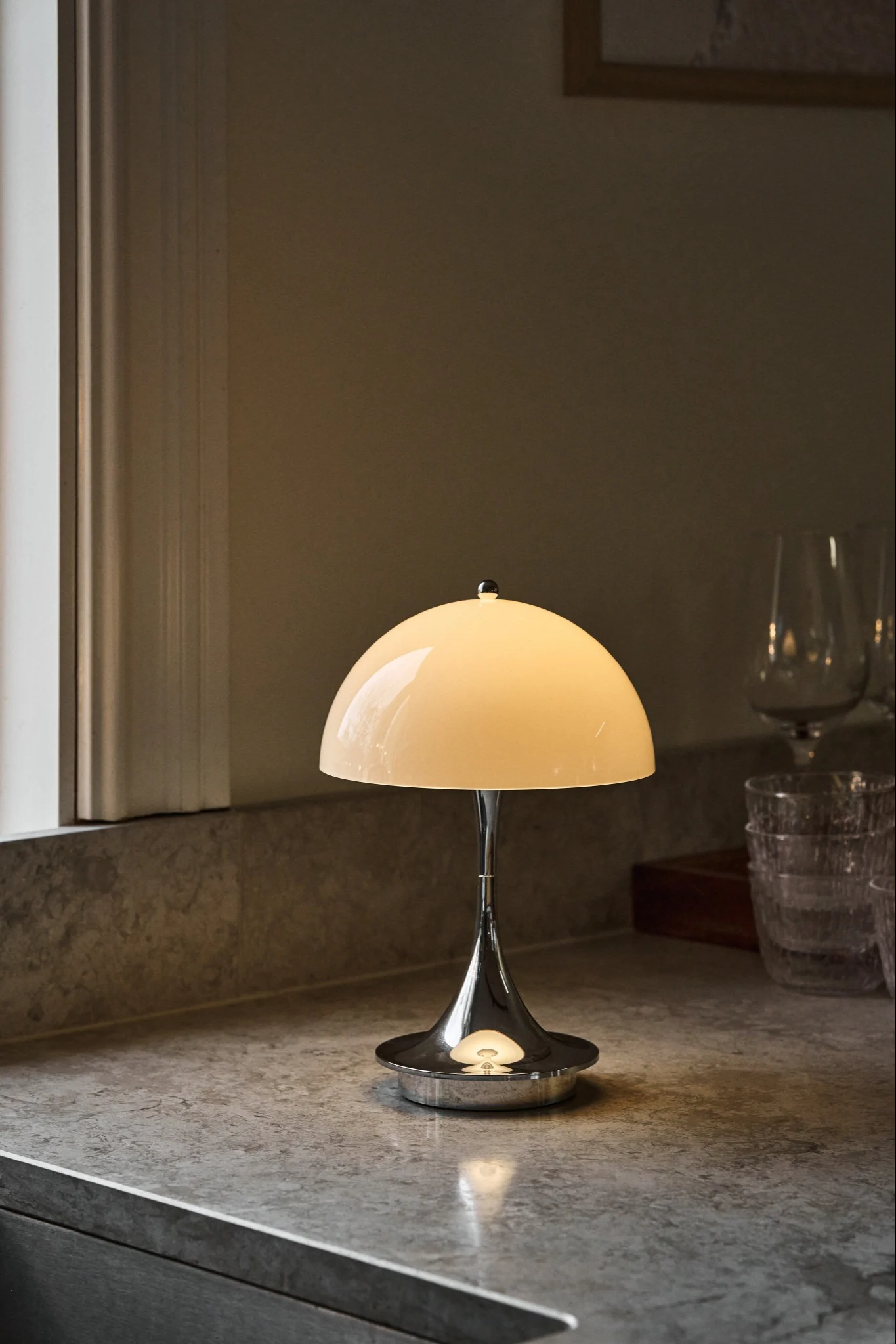 En Panthella bordslampa i beige och kromfot står i ett kök och lyser. Lampan är klassisk designlampa.