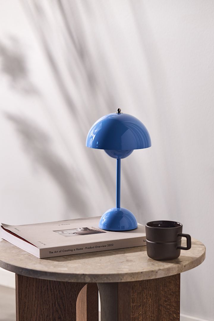 Flowerpot portable bordslampa VP9 i en klar blå färg står på ett sidobord i trä som står mot en naturvit vägg. 