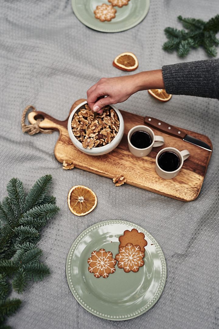 Glögg står serverad ur glöggmuggar från ERNST och pepparkakor vilar på grön assiett på glöggminglet i skogen. 