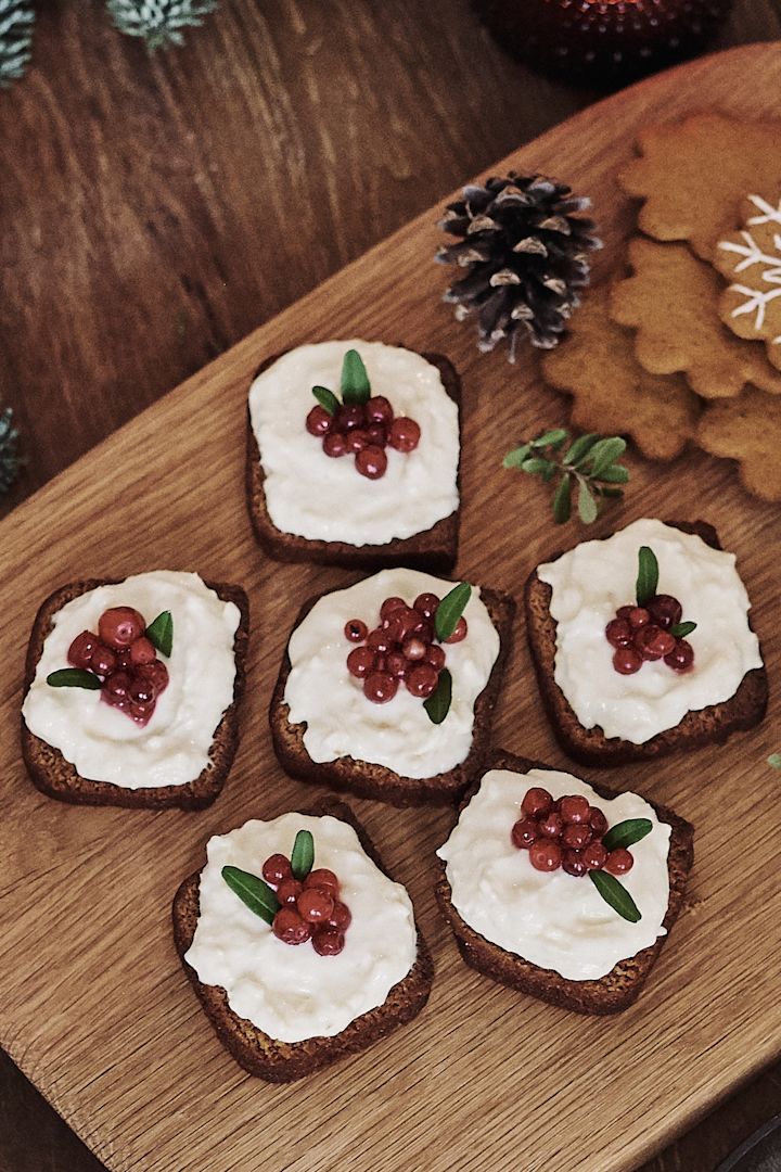 Mjuk pepparkaka med frosting och dekorerad med lingon står serverad på bordet på en snygg skärbräda till adventsmyset. 