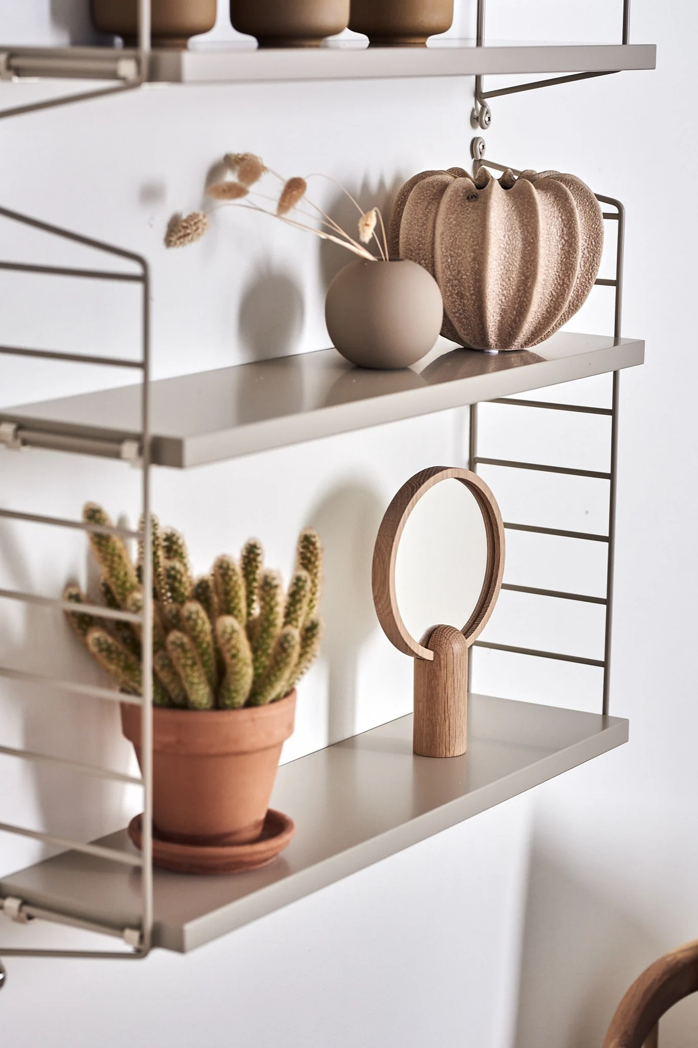 String Pocket-hylla i beige färg stylad med trendiga inredningsdetaljer som sandfärgade vaser.