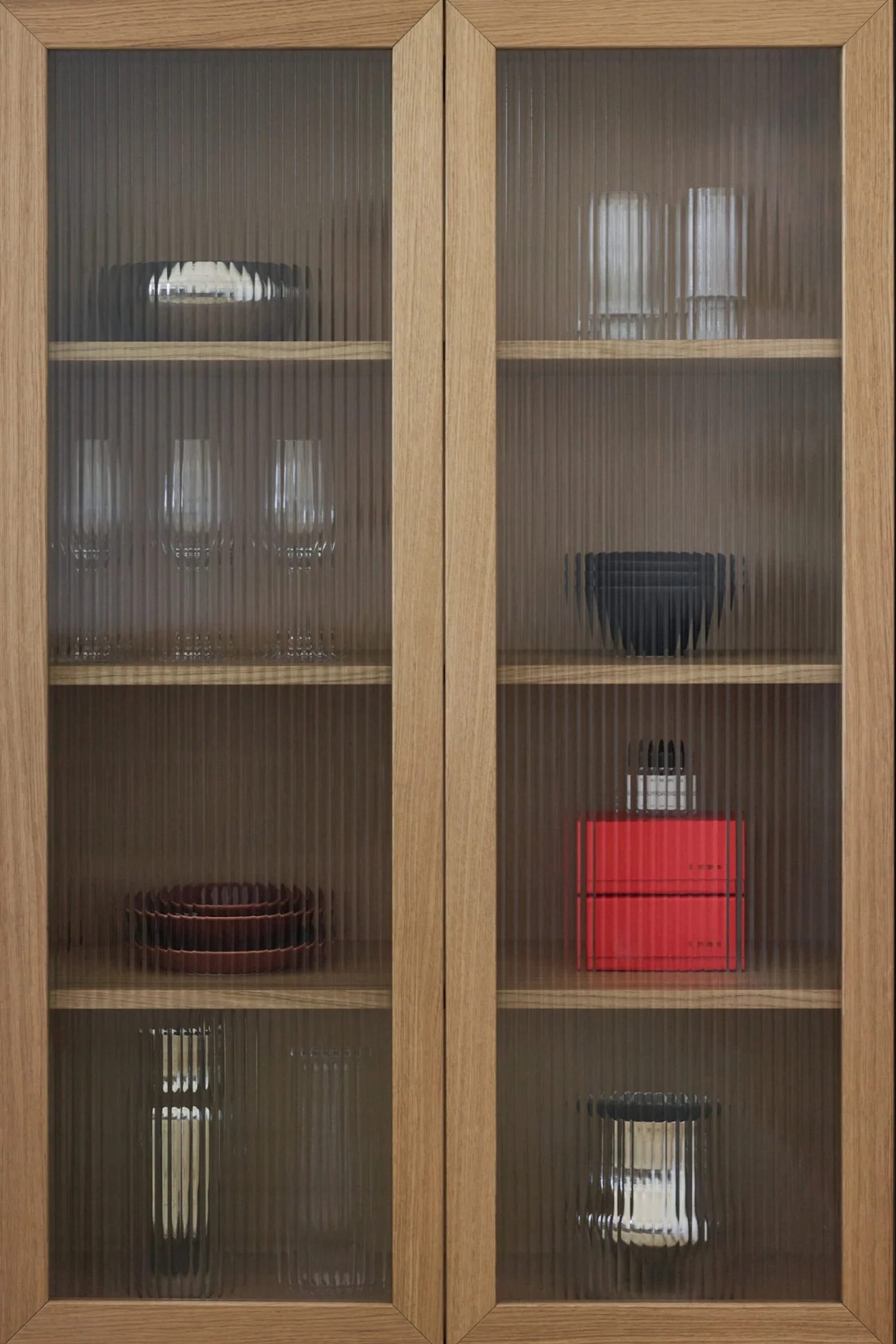 Träskåp med räfflade glasdörrar, som visar olika fat, glas och dekorativa föremål på hyllorna.