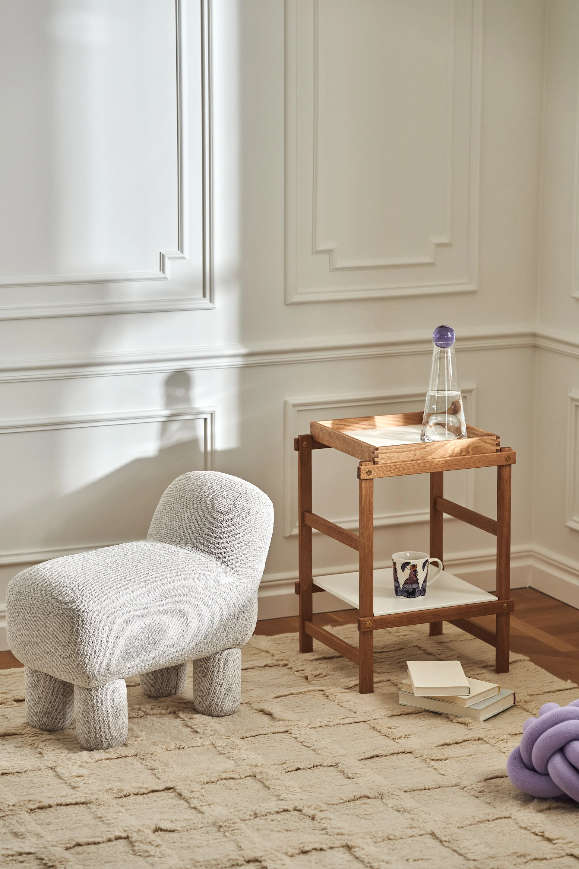 Stilrent vardagsrum med produkter från Design House Stockholm i form av Lulu-sittpuff, Frame-hylla i ek, Knot-kudde i lavendelfärg och Elsa Beskow-mugg. 