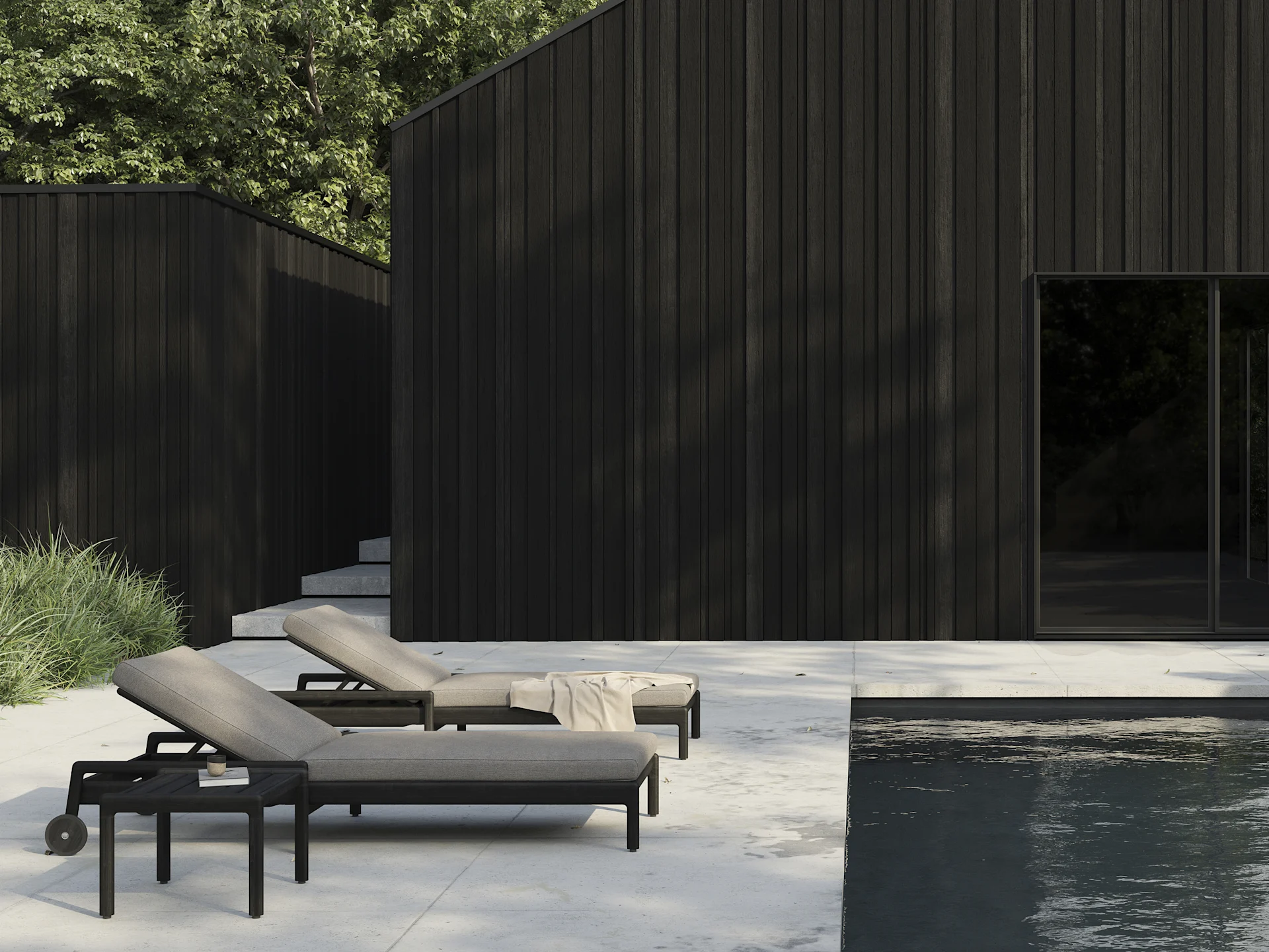 Två mörka solstolar med ljusa dynor på en uteplats vid en pool, med moderna mörka träbyggnader i bakgrunden.