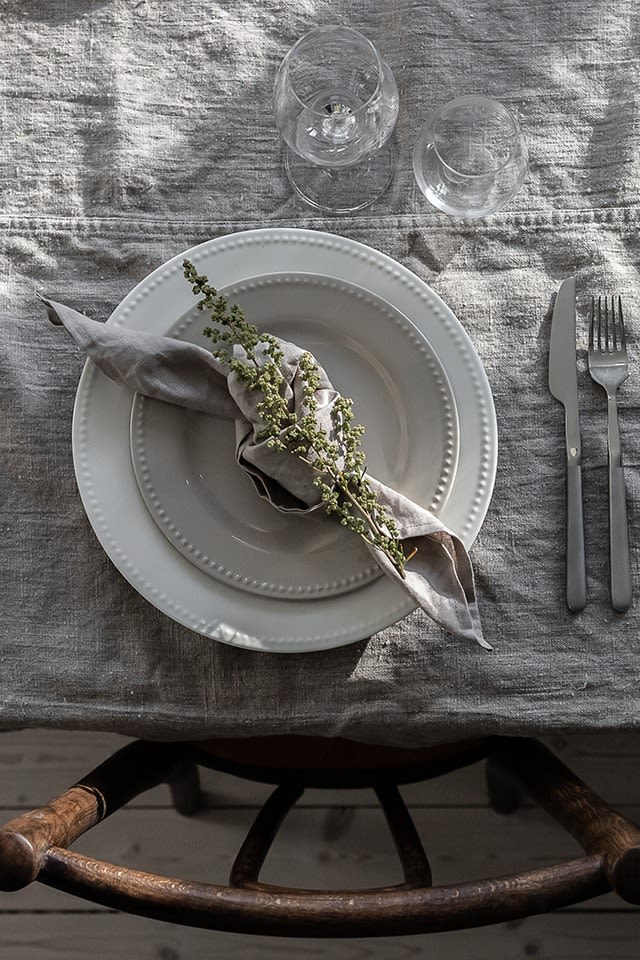 Linneservett i färgen sand från Nordic Nest i en knuten servettvikning, här dekorerad med en blommande kvist. 