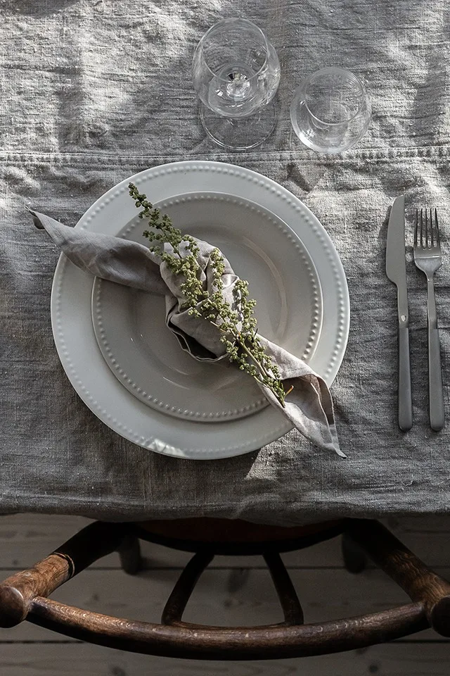Linneservett i färgen sand från Nordic Nest i en knuten servettvikning, här dekorerad med en blommande kvist.