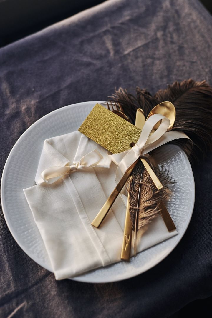 En servettvikning i form av en skjorta till nyår ligger på tallriken med bestick, placeringskort och dekorativ fjäder. 