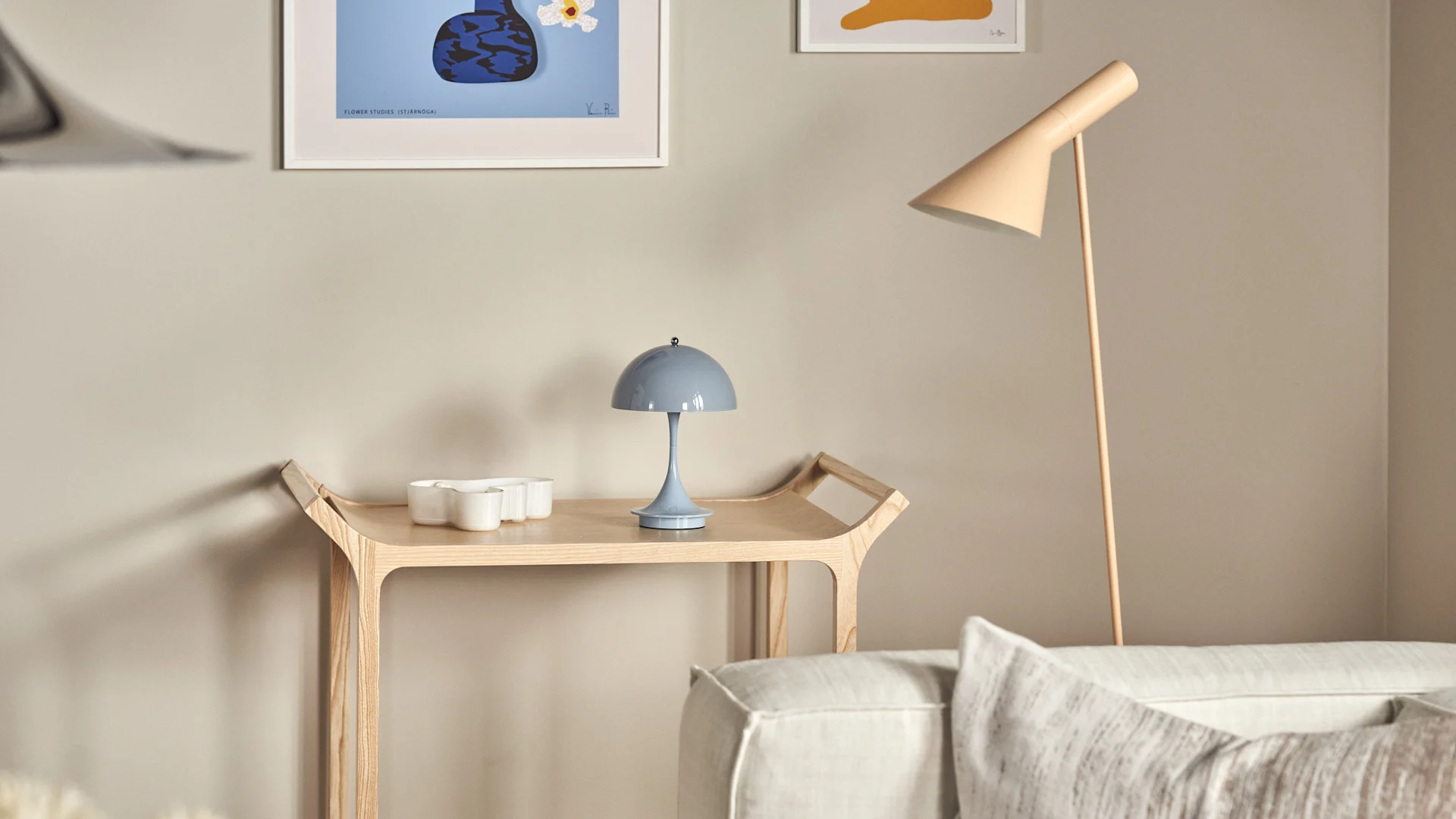 Panthella portabel bordslampa tillsammans med AJ golvlampa är en fin kombination, här i ljusblått och beige i vardagsrumsmiljö med beige soffa och rullvagn i trä.