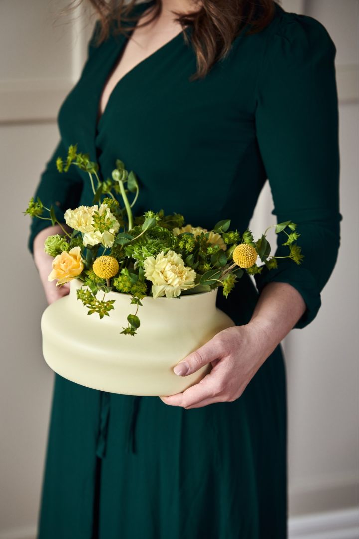 Händer som håller Dorotea vas i färgen mellow yellow från Gense, formgiven av Monica Förster. I vasen ser du en gul bukett med rosor och gröna kvistar.