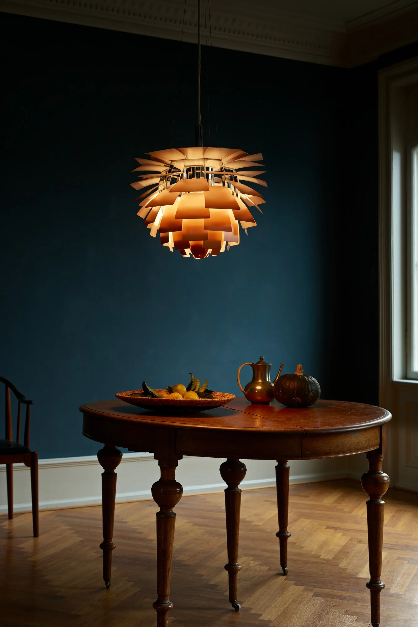 En PH artichoke taklampa som hänger över ett bord med en mörkblå bakgrund. Lampan tillhör en klassisk designlampa. 