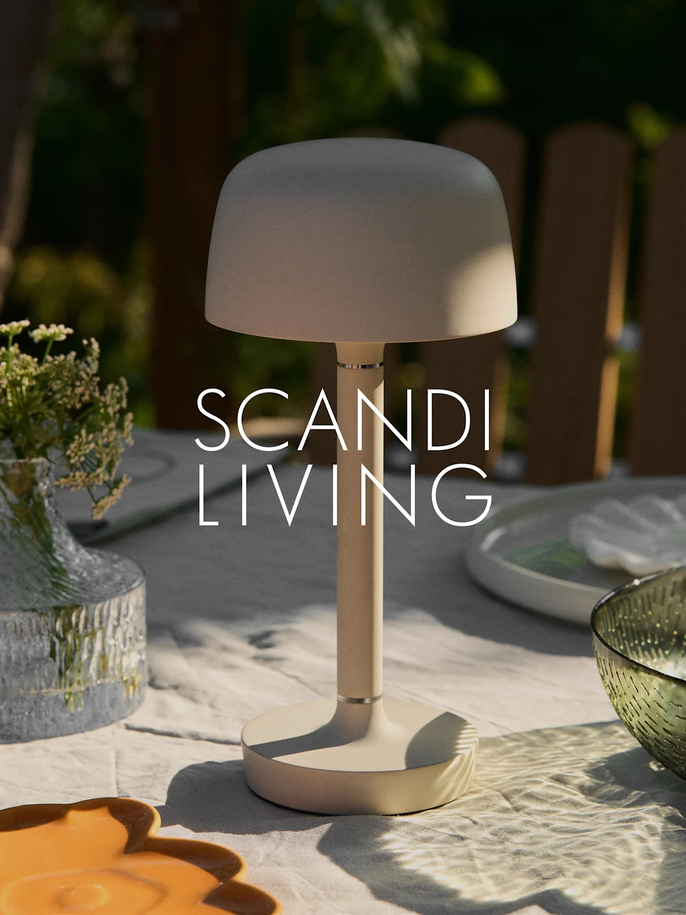 En beige modern bärbar bordslampa på ett utomhusbord med en vas blommor och fat. Texten "SCANDI LIVING".