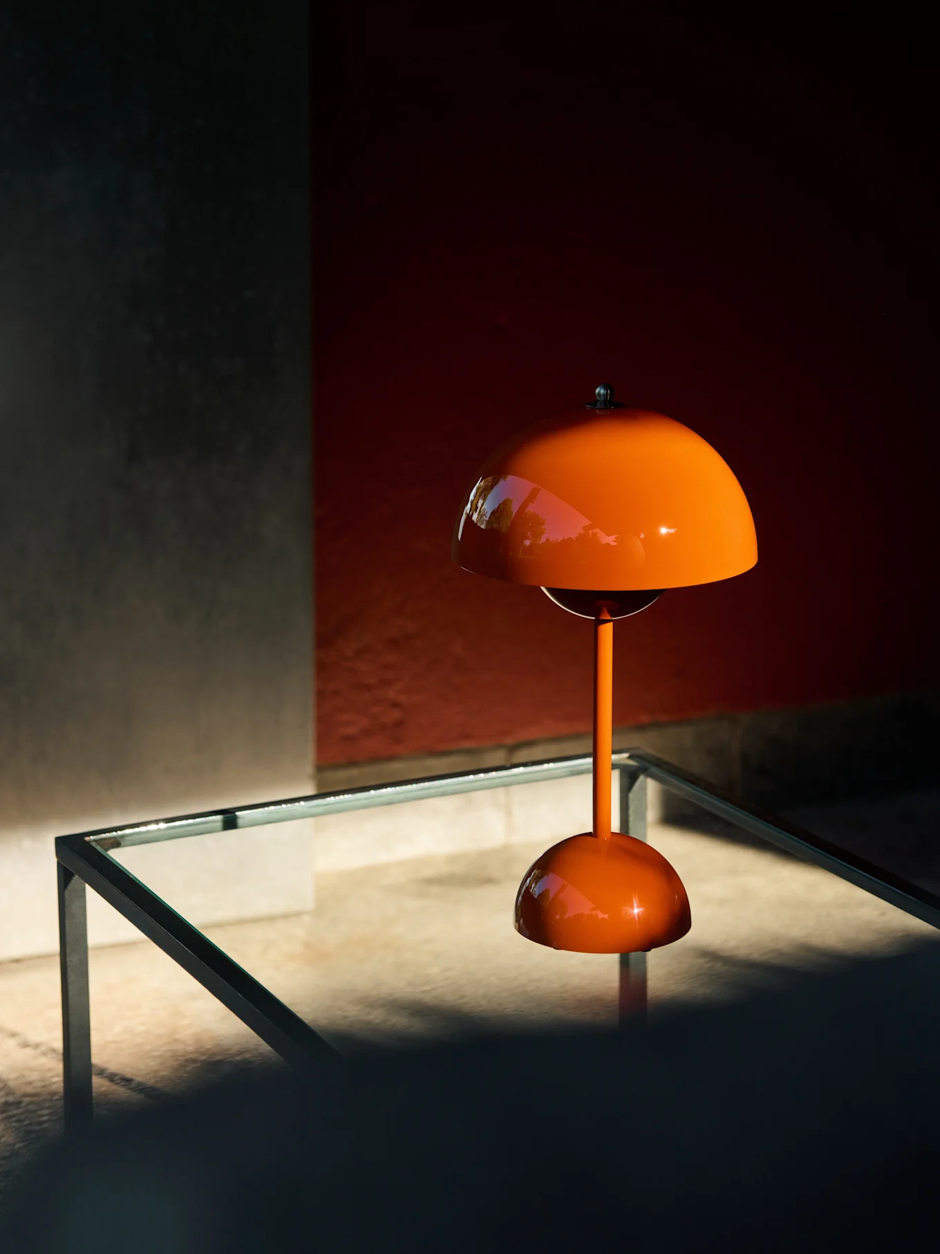Orange svampformad bordslampa på ett glasbord, som reflekterar grönska.