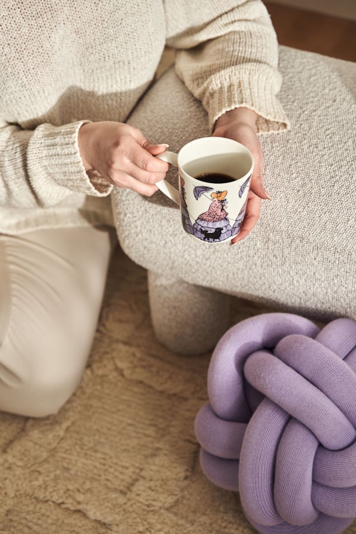 Mugg med Elsa Beskow-motivet Tant Gredelin från Design House Stockholm samt Fia-karaff i glas med lila lock på Frame-hylla i ek och vitt. 