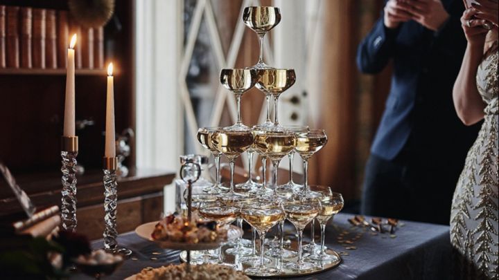 Ett högt champagnetorn med kupade champagneglas står på nyårsfestens mingelbord. 