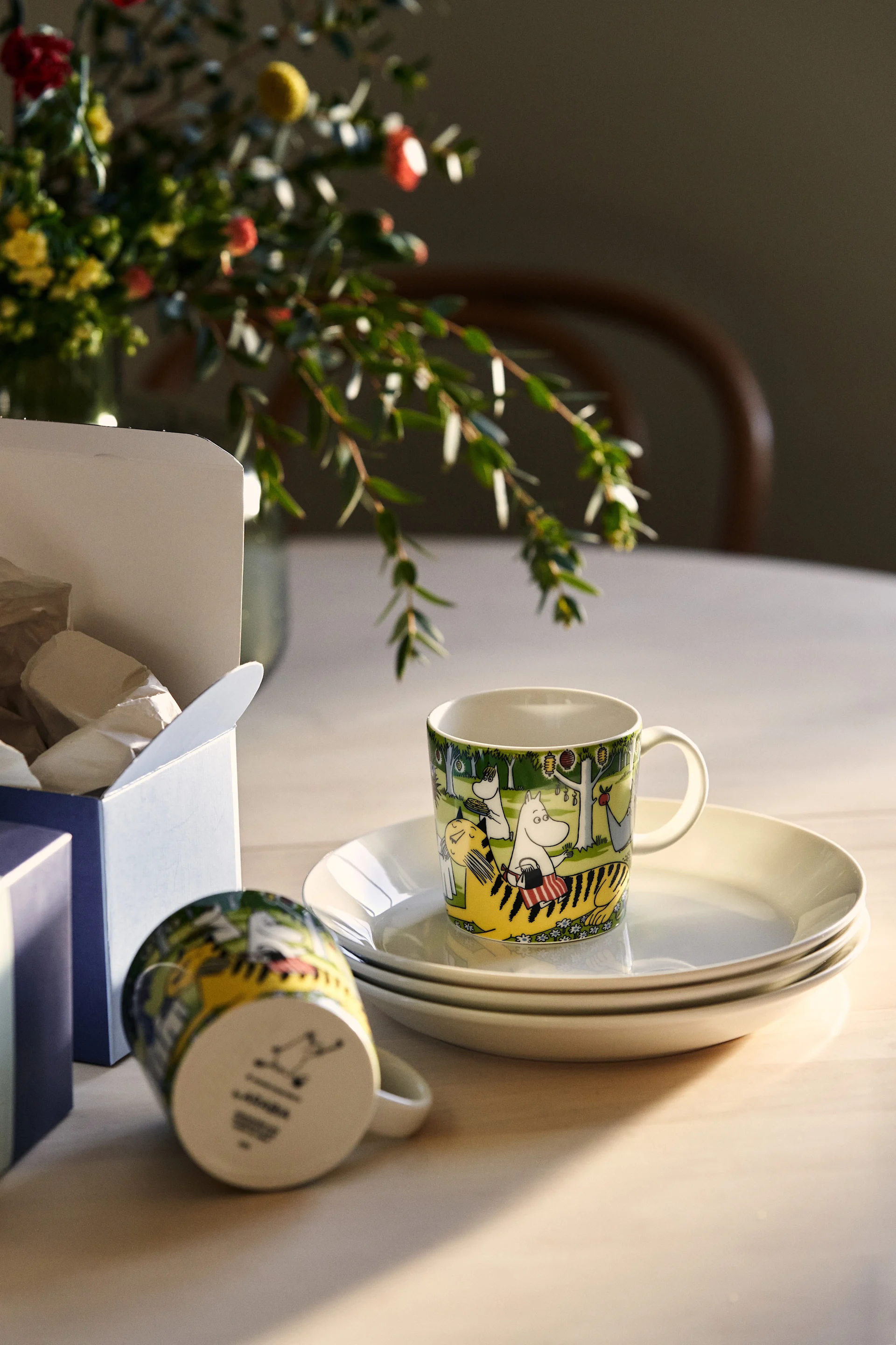 Två muminmuggar i kollektionen Garden Party ligger uppackade från sina kartonger på ett köksbord i ljust trä.