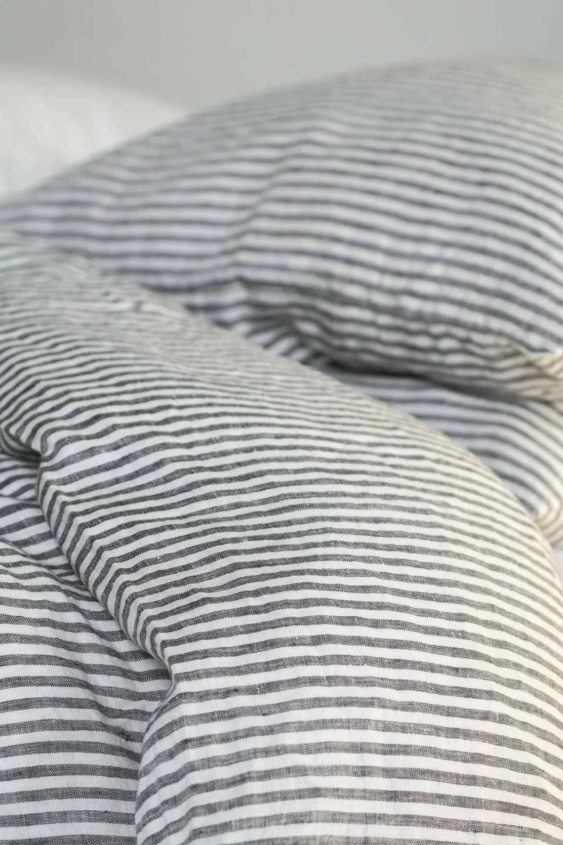 Närbild av en skrynklig säng med svart- och vitrandiga sängkläder i linne.