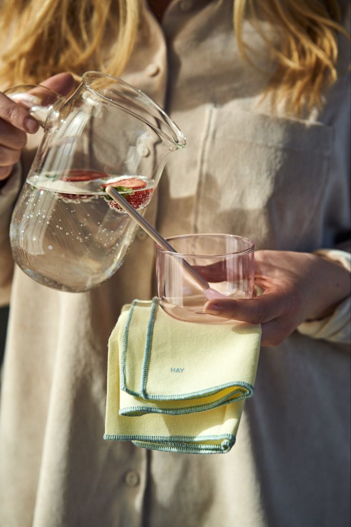 Häller jordgubbsvatten ur Jug S Kanna i rosa Tint glas med rosa Round glassked i, tillsammans med gul Contour tygservett i färgen Lemon i handen från HAY.