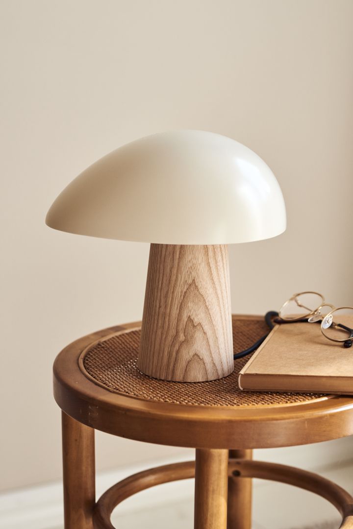 Förnya ditt hem med trendiga lampor - här ser du Fritz Hansen Night Owl bordslampa i vitt och ljust trä på en pall av rotting.