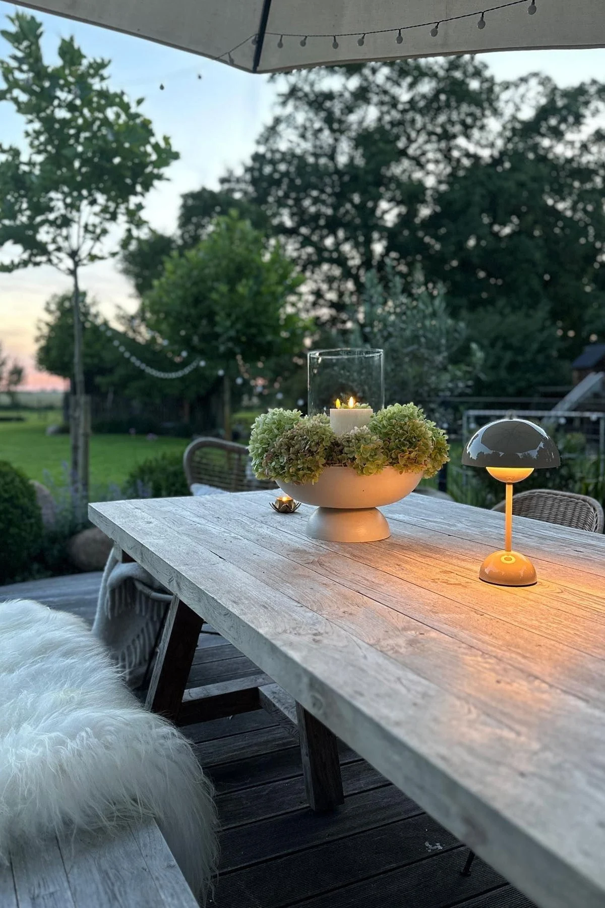 En mysig terrass med ett stort matbord och bänkar, inredd med levande ljus och en Flowerpot bordslampa från &Tradition.