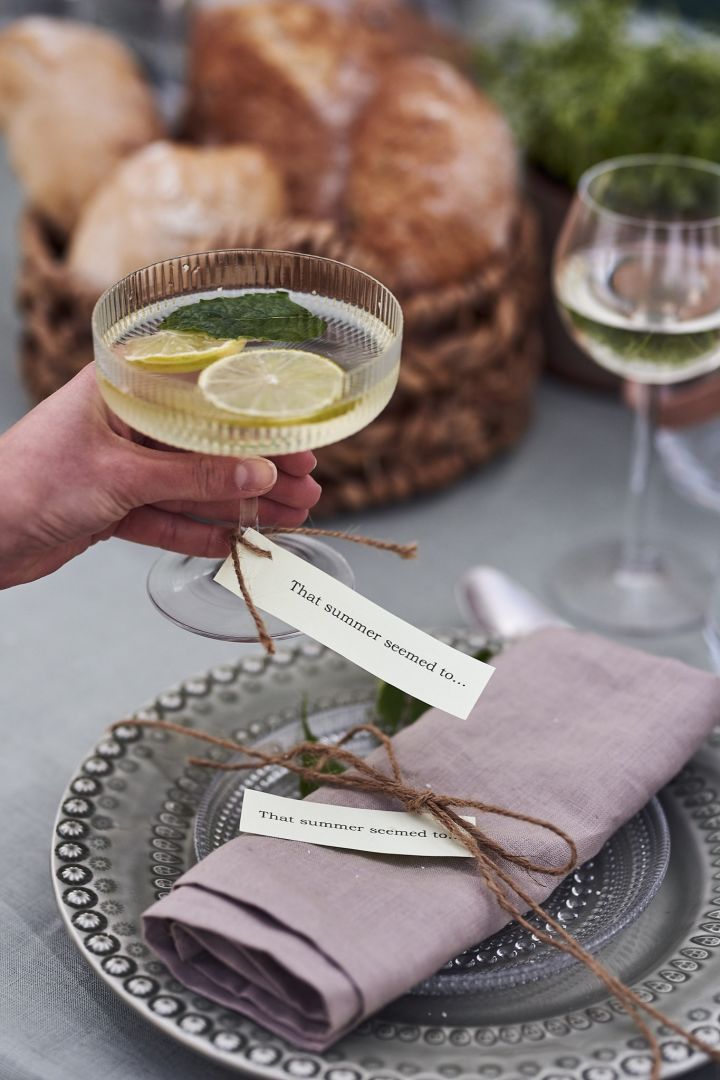 Somrigt placeringskort i form av sommarlåt på lapp knuten runt champagneglaset och servetten på bordet. 