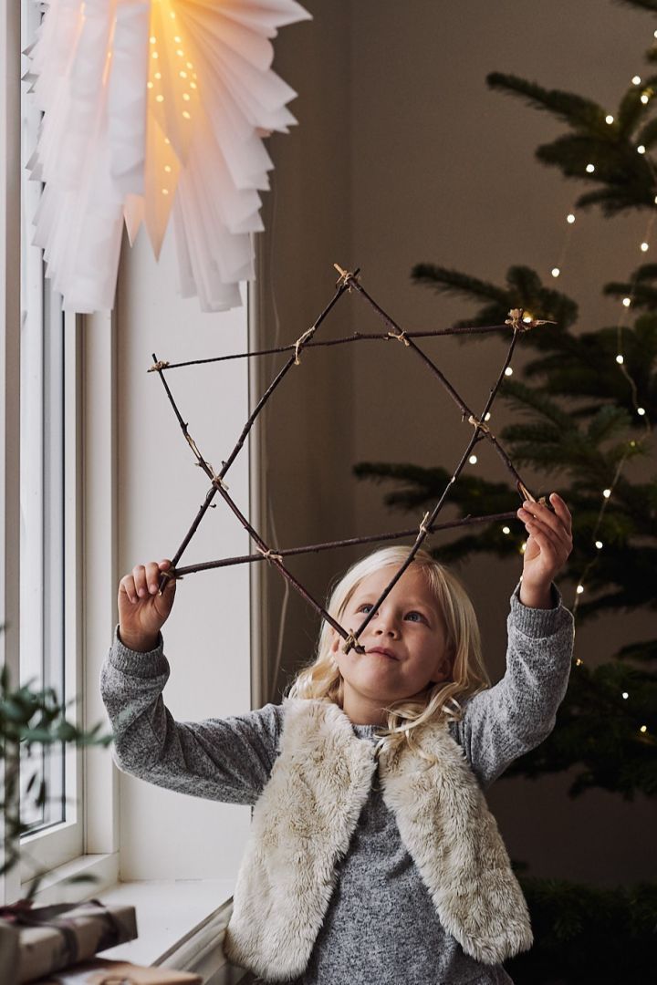 Barnet vill hänga upp sin egengjorda julstjärna av pinnar bredvid den stilrena Snöblomma i fönstret. 