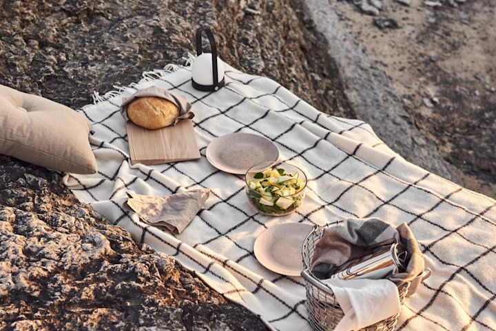 Njut av en picknick på stranden vid solnedgång med olika tilltugg, en pläd och portabel belysning - här lampan Carrie i svart från Audo Copenhagen. 