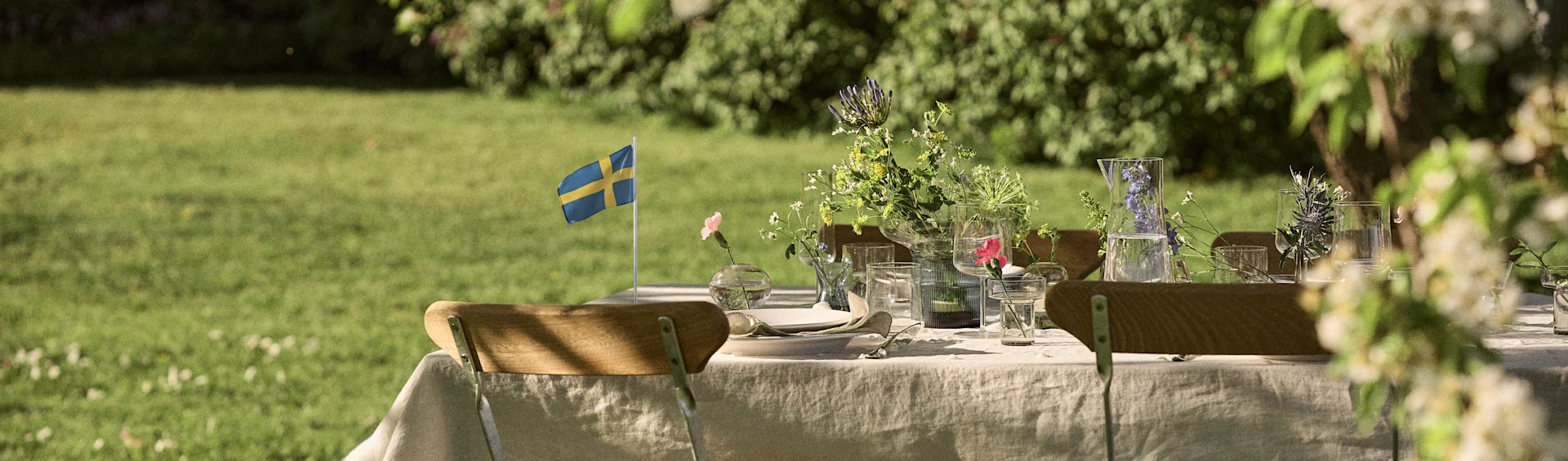 Utedukning med vildblommor, glasvaror och en svensk flagga i en trädgård.