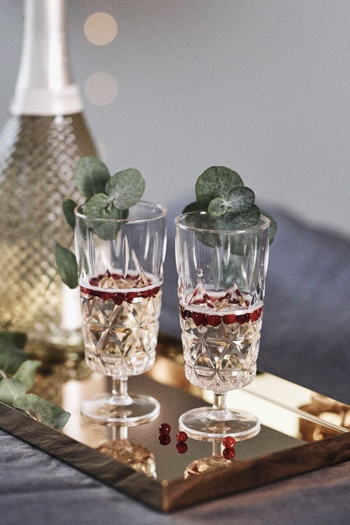 Nyårsdrink med champagne, lingon och eukalyptuskvist på glaskanten i champagneglas i plast från Sagaform. 