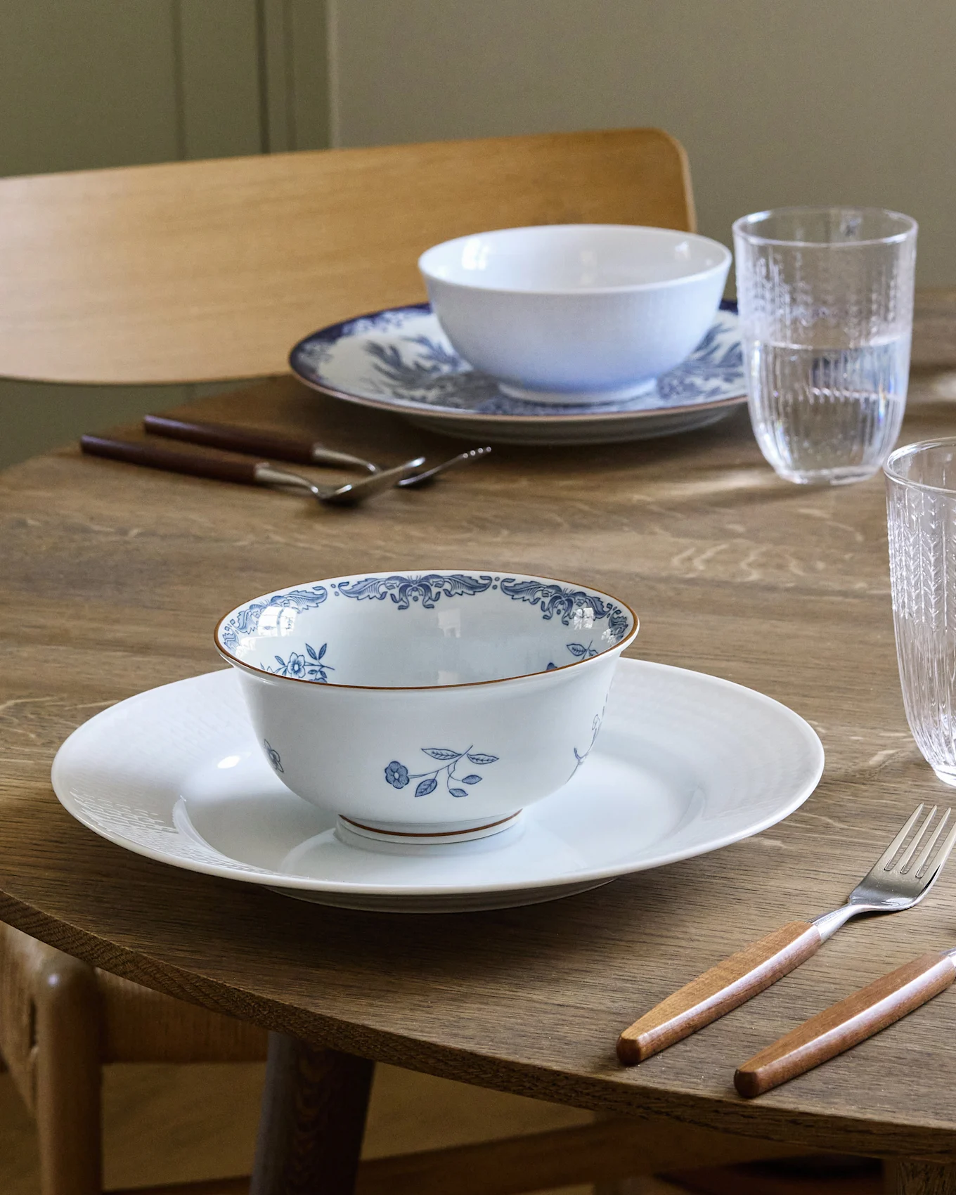 Matbord dukat för två med vita och blåmönstrade skålar på vita tallrikar, bestick med trähandtag och vattenglas.