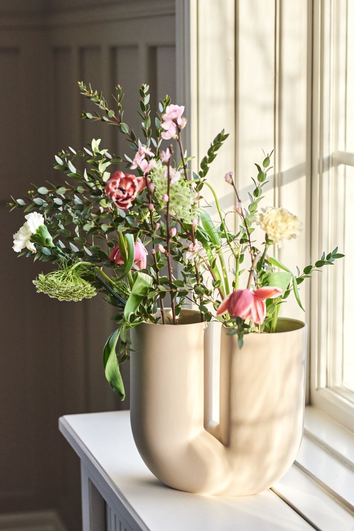 Runda och lekfulla Kink vas i färgen Sand från Muuto som står på fönsterbrädan är en av säsongens stora vaser för vårens blomster.