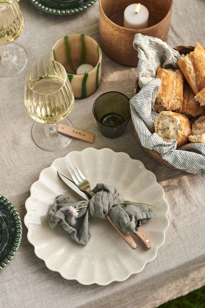 Duka till midsommar - här uppdukat med beige Oyster tallrik från Mateus, bestick inlindade i en tygservett och vitvinsglas på ett dukat bord. 
