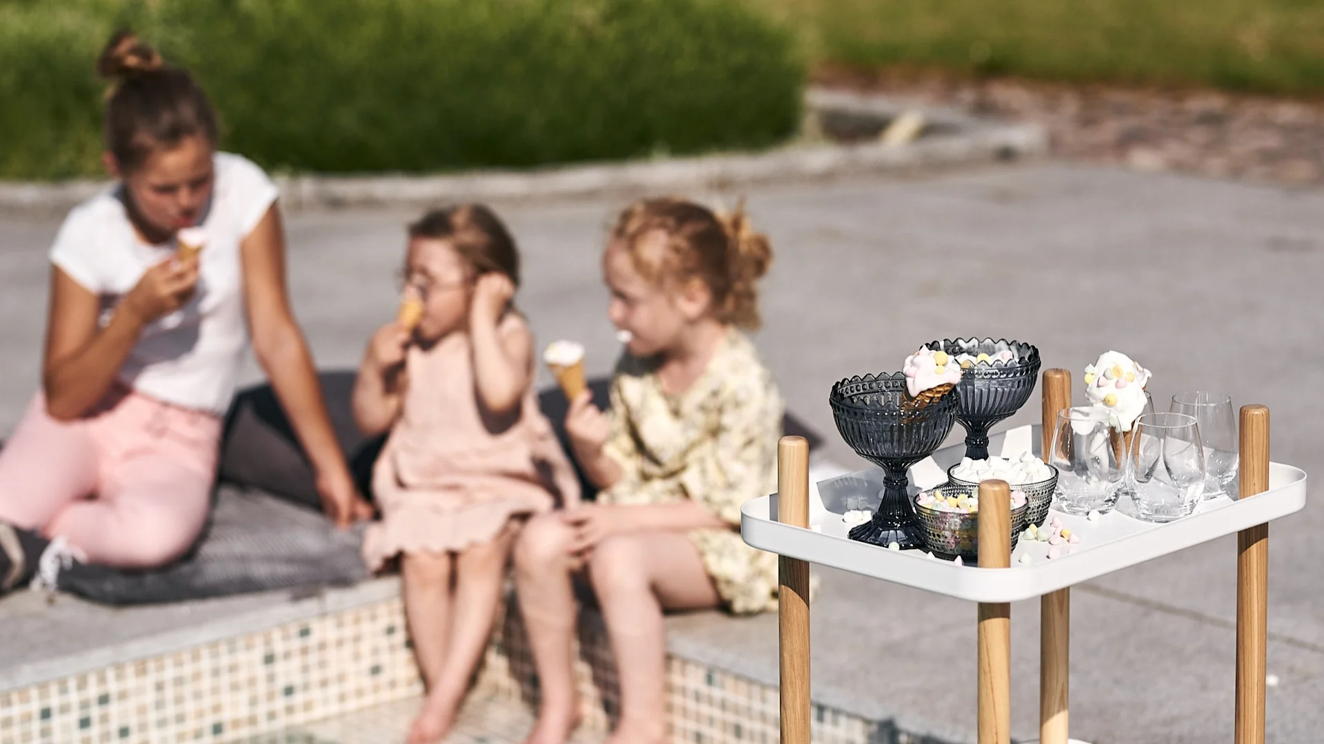 På ett vitt brickbord från Normann Copenhagen står skålar från Iittala fyllda med goda glasstillbehör att avnjuta vid poolen.