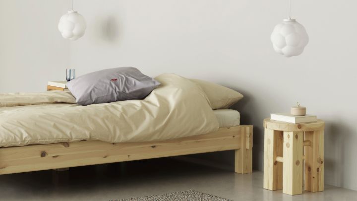 Bubba taklampa från Normann Copenhagen är en modern, vit sovrumslampa med bubblig design. Lampan ger sovrummet en modern känsla och sprider ett mjukt sken, här i sovrum med säng i obehandlat trä och ljusgula sängkläder.