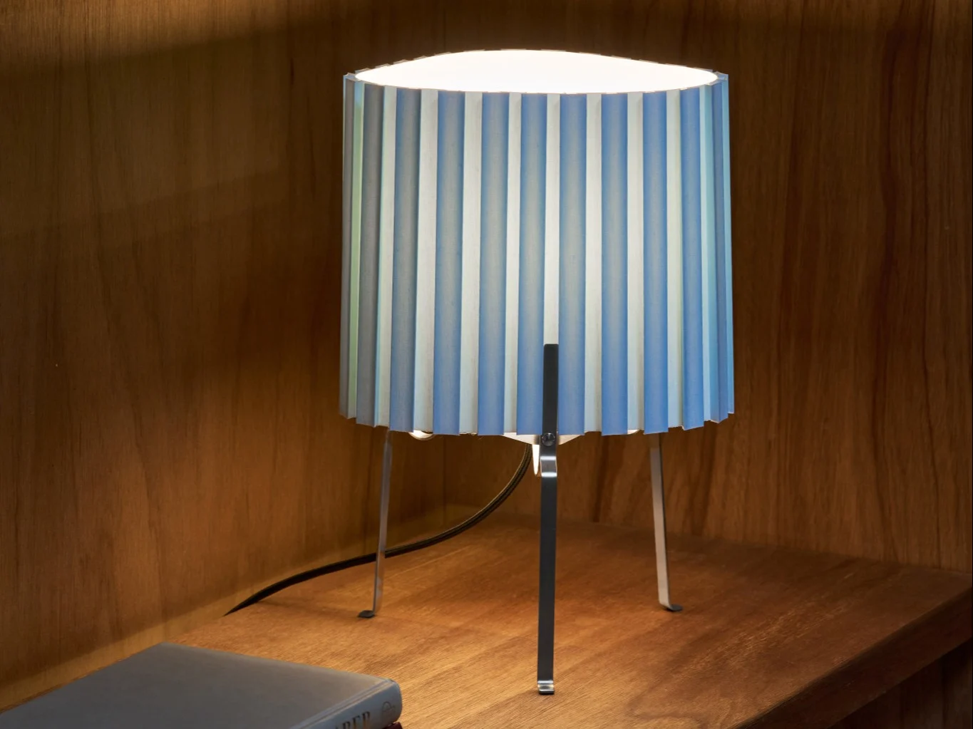 Bordslampa med veckad blå- och vitrandig skärm på en trähylla, som lyser upp området.