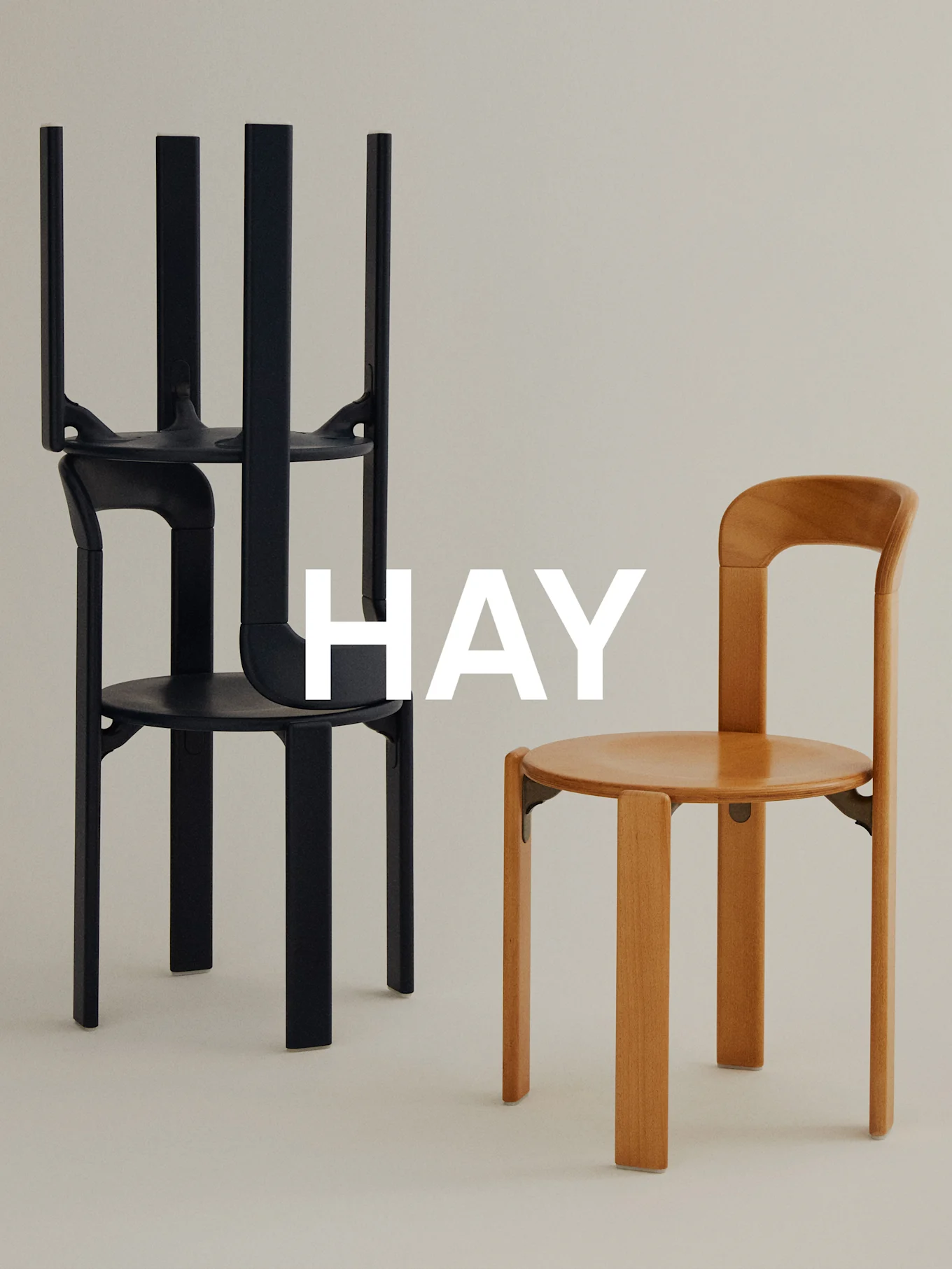 Två minimalistiska stolar mot ljus bakgrund, en svart staplad, en ljusbrun upprätt, med 'HAY' överlägg.