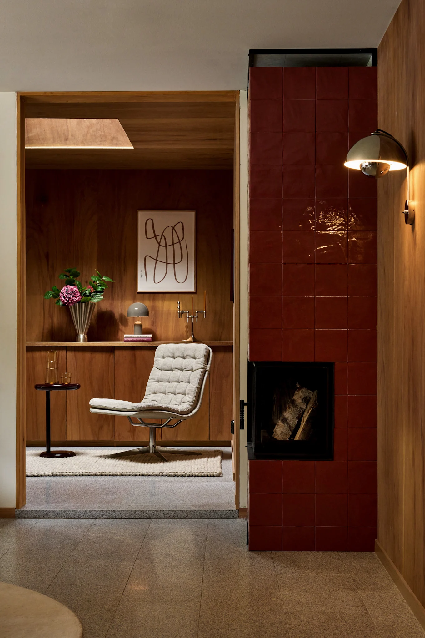 En mysig interiör med en texturerad loungestol, träpaneler, en rödkaklad öppen spis och en gyllene vägglampa.