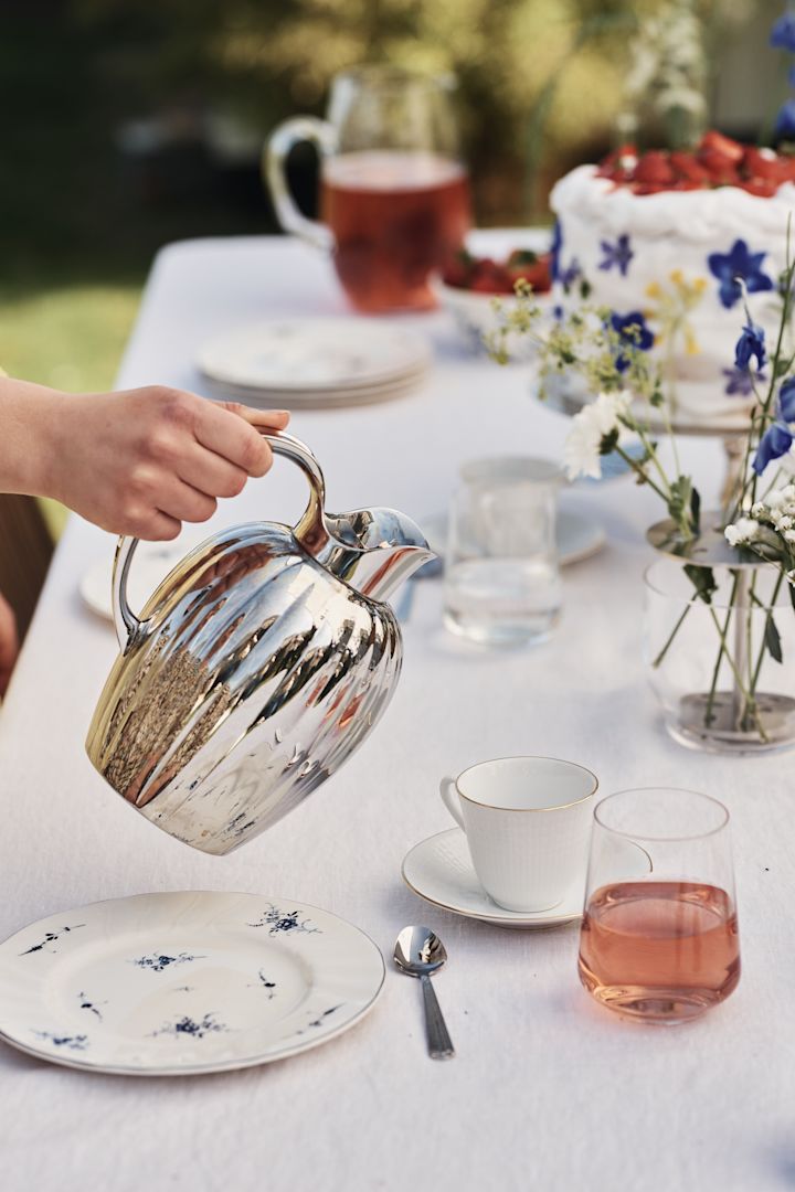 Låt det rostfria stålet komma igen i detaljer i den blåvita midsommardukningen, här serveras kaffet ut den klassiska Bernadotte termoskannan i rostfritt stål från Georg Jensen.