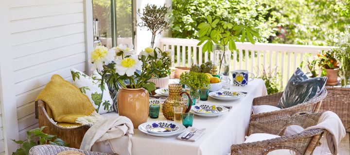 En medelhavsinspirerad sommarlunch står uppdukad på verandan, i toner av gult, grönt och blått med porslin från Arabia och glas från Iittala.
