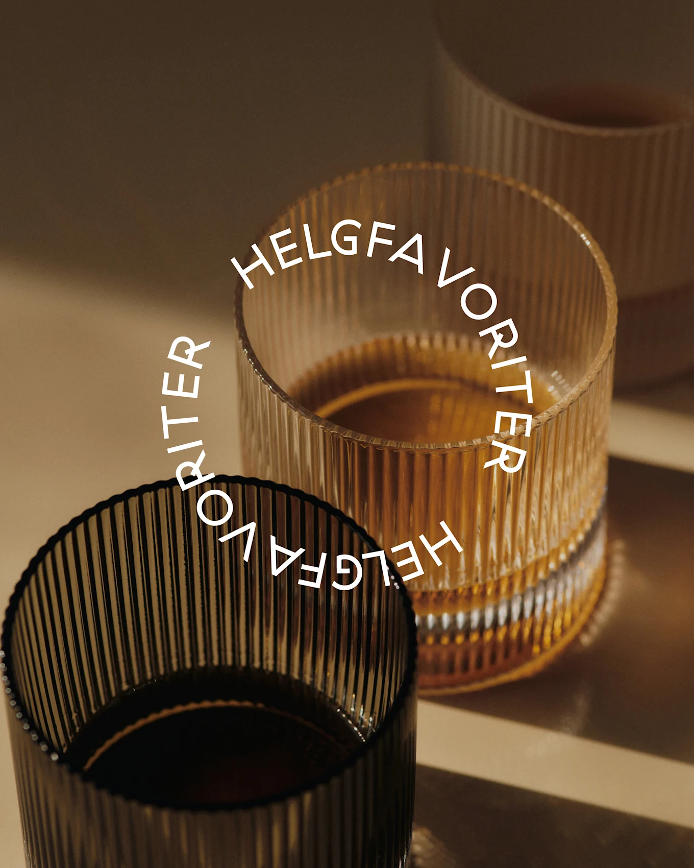 Tre räfflade glas med dryck, två fyllda med gulaktig vätska och ett med mörk vätska, med texten 'HELGFAVORITER' i en cirkel.