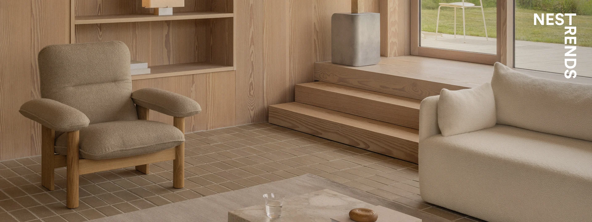 Ett modernt vardagsrum med en texturerad brun fåtölj, en beige soffa, träpaneler, klinkergolv och utsikt mot en trädgård.