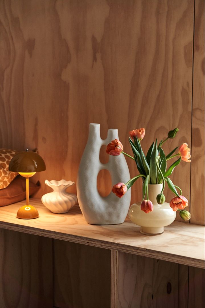 En avsats med en portabel lampa, en skulptur och en vas med färska blommor skapar ett visuellt intresse i rummet. 