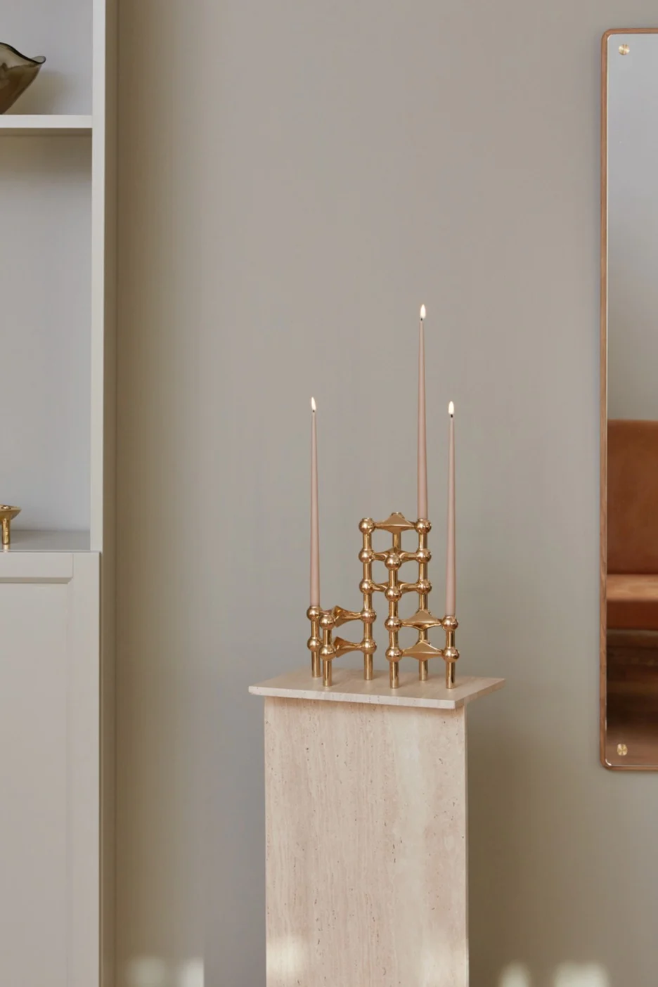 En mässing ljusstake står på en pedestal med tre tända ljus. 