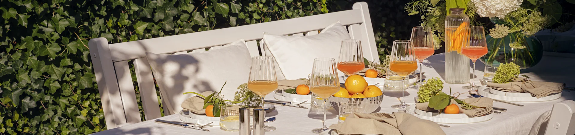 Utebord dukat för sommarbuffé med vita räfflade tallrikar, linnedukar, räfflade glas med dryck, citroner och mandariner.