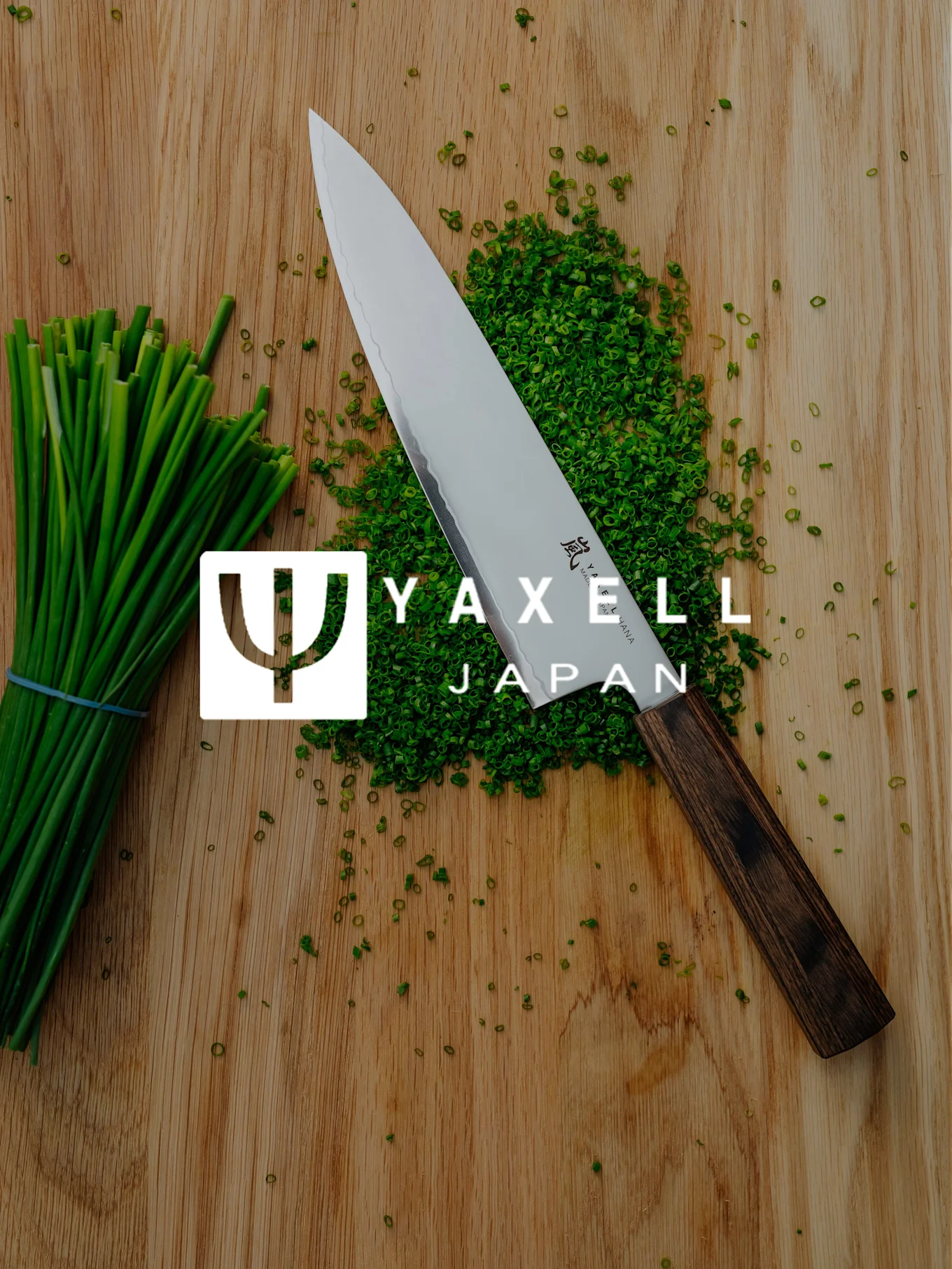 Yaxell kockkniv, hackad gräslök och en bunt gräslök på en träskärbräda med Yaxell Japan-logotyp.