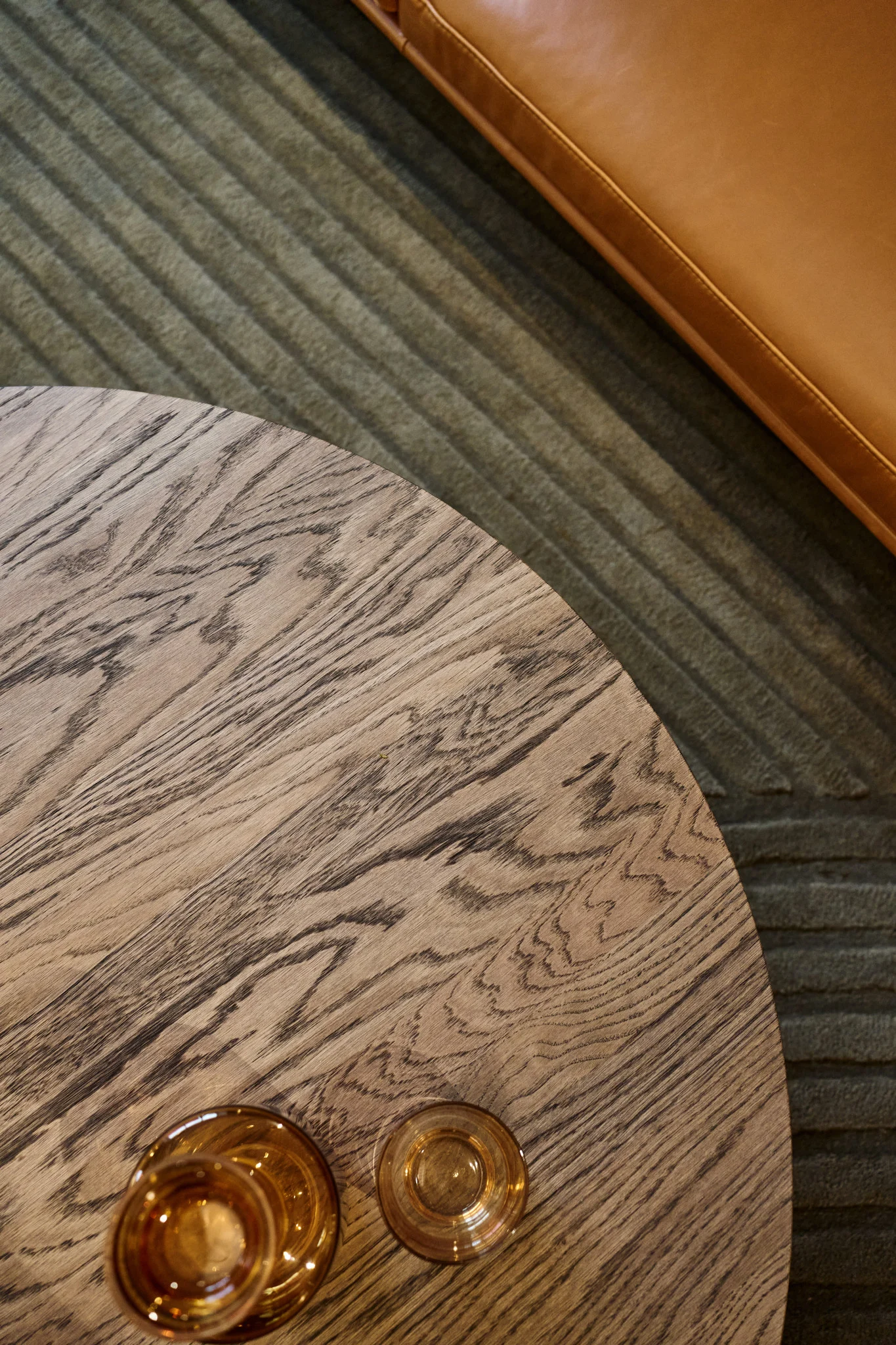 Ett soffbord med en mörkbrun bordsskiva står framför en soffa, med olika bärnstensfärgade glas från Raise-kollektionen från Muuto ovanpå.