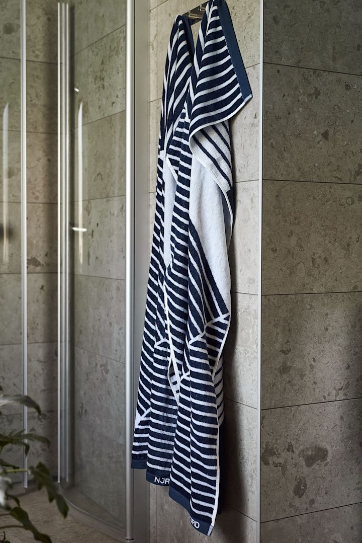 Ge bort badhandduken Stripes från NJRD som en farsdagspresent till bastuälskare, här hängande framför en dusch. 