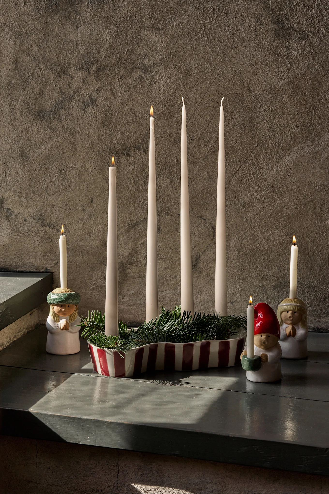 Adventsdekoration med fyra otända ljus, grön granris och tre figurer som håller tända ljus.