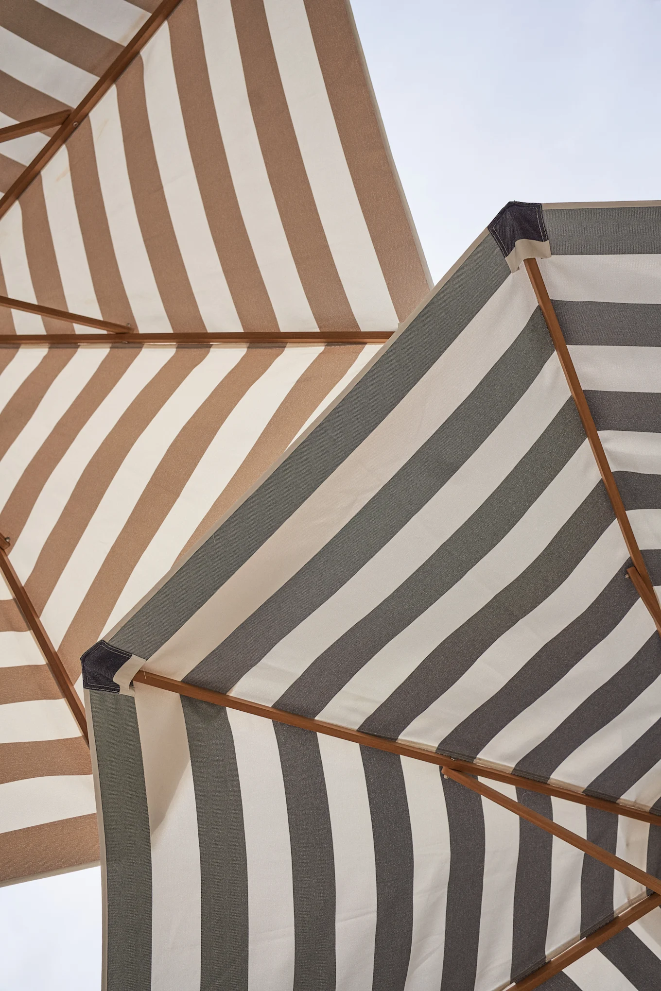 Två randiga strandparasoller sedda underifrån, en brun och vit, den andra grå och vit, mot en ljus himmel.Inspiration till din balkong 2026.