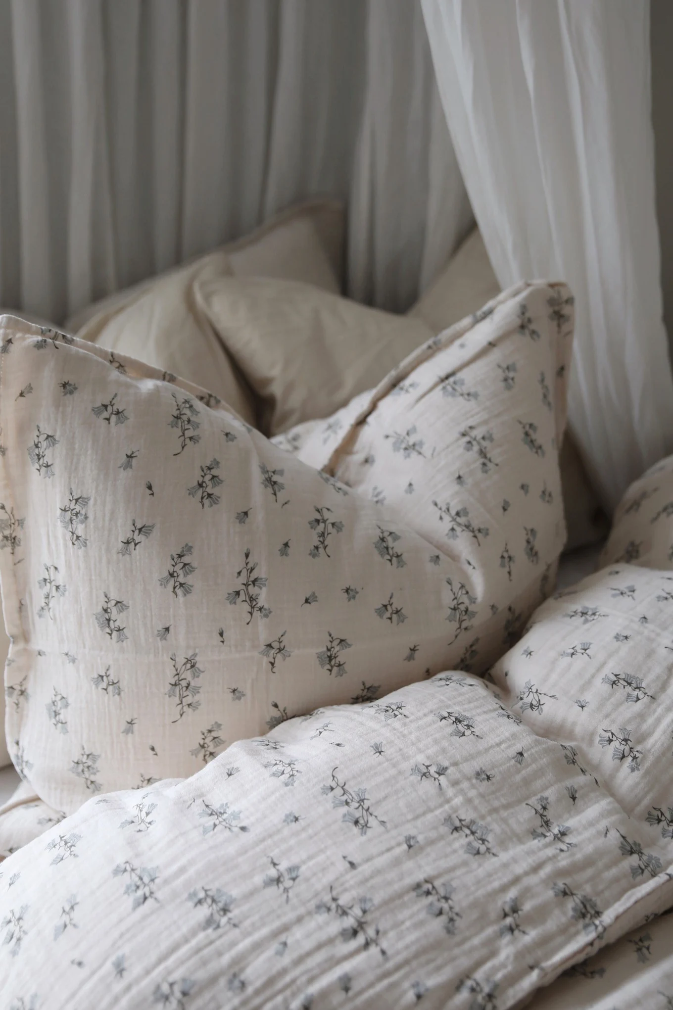 Mysiga sängkläder i ljusbeige krinklat tyg med ett delikat blått blommönster och vita gardiner.