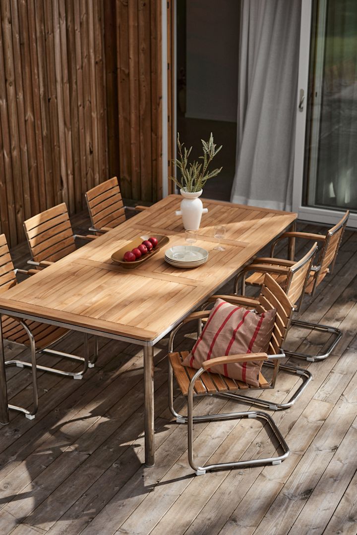 En terrass med en mysig matplats som består av Rörvik-kollektionen från 1898, ett bord dekorerat med en vas och en kudde på en stol.